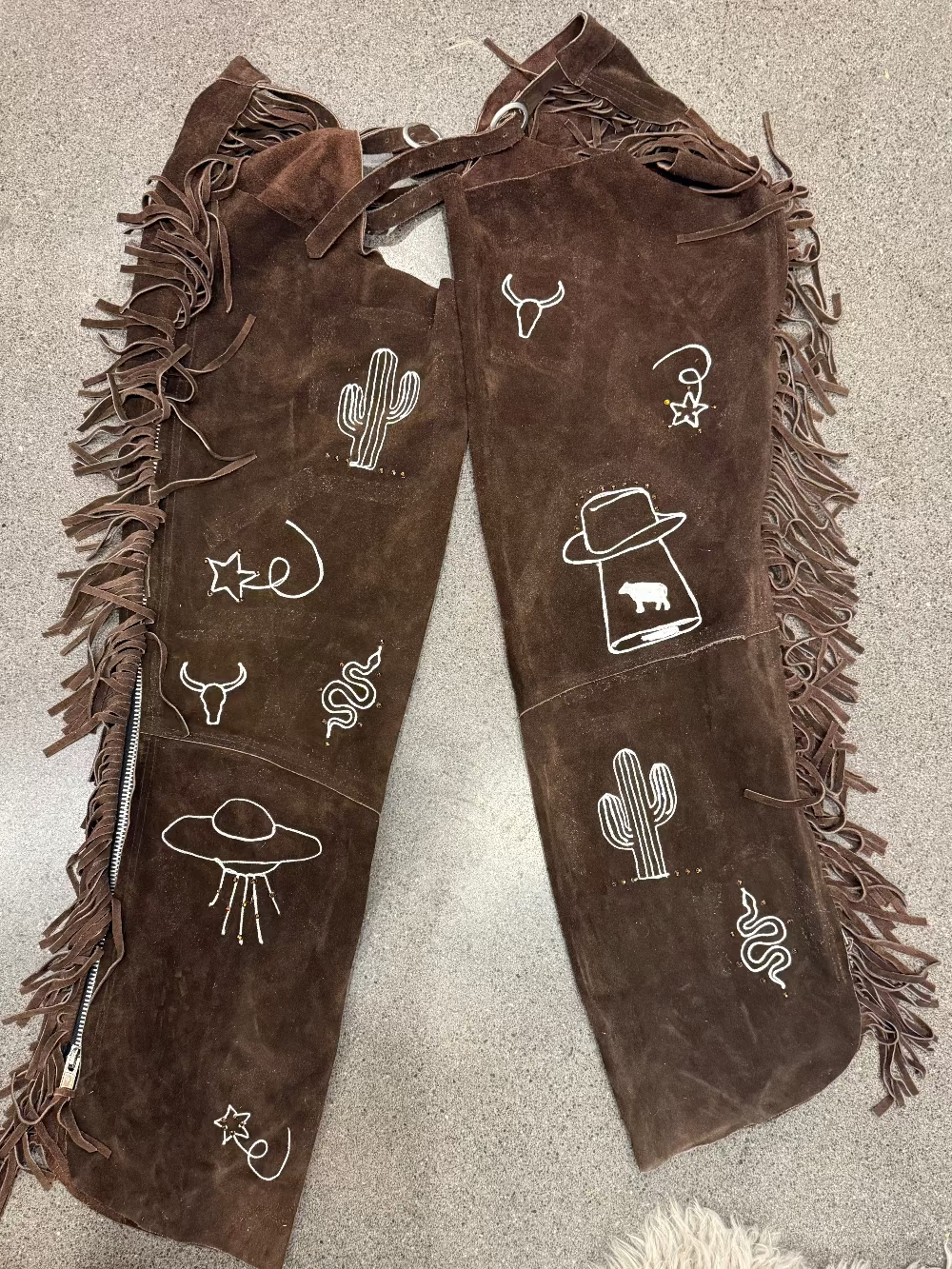 Brown fringed boots with white embroidered designs on a beige surface