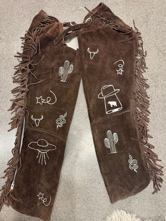 Brown fringed boots with white embroidered designs on a beige surface