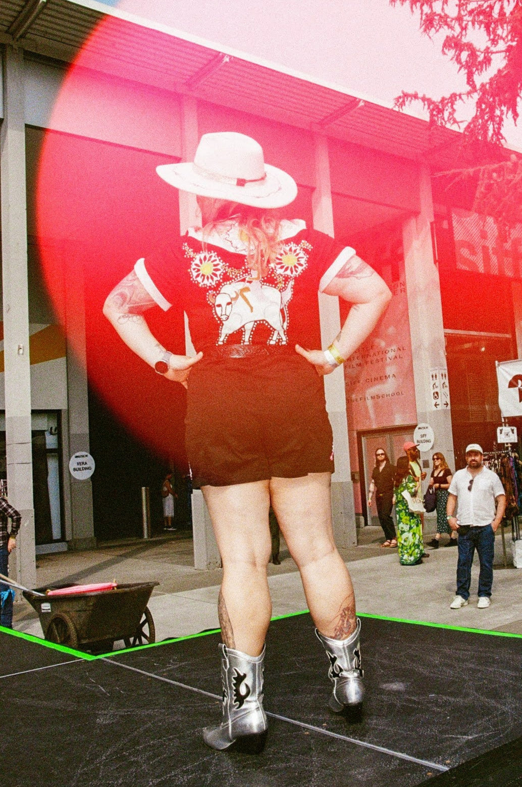 Person on a stage with a red circular overlay, outdoor setting with people and buildings.